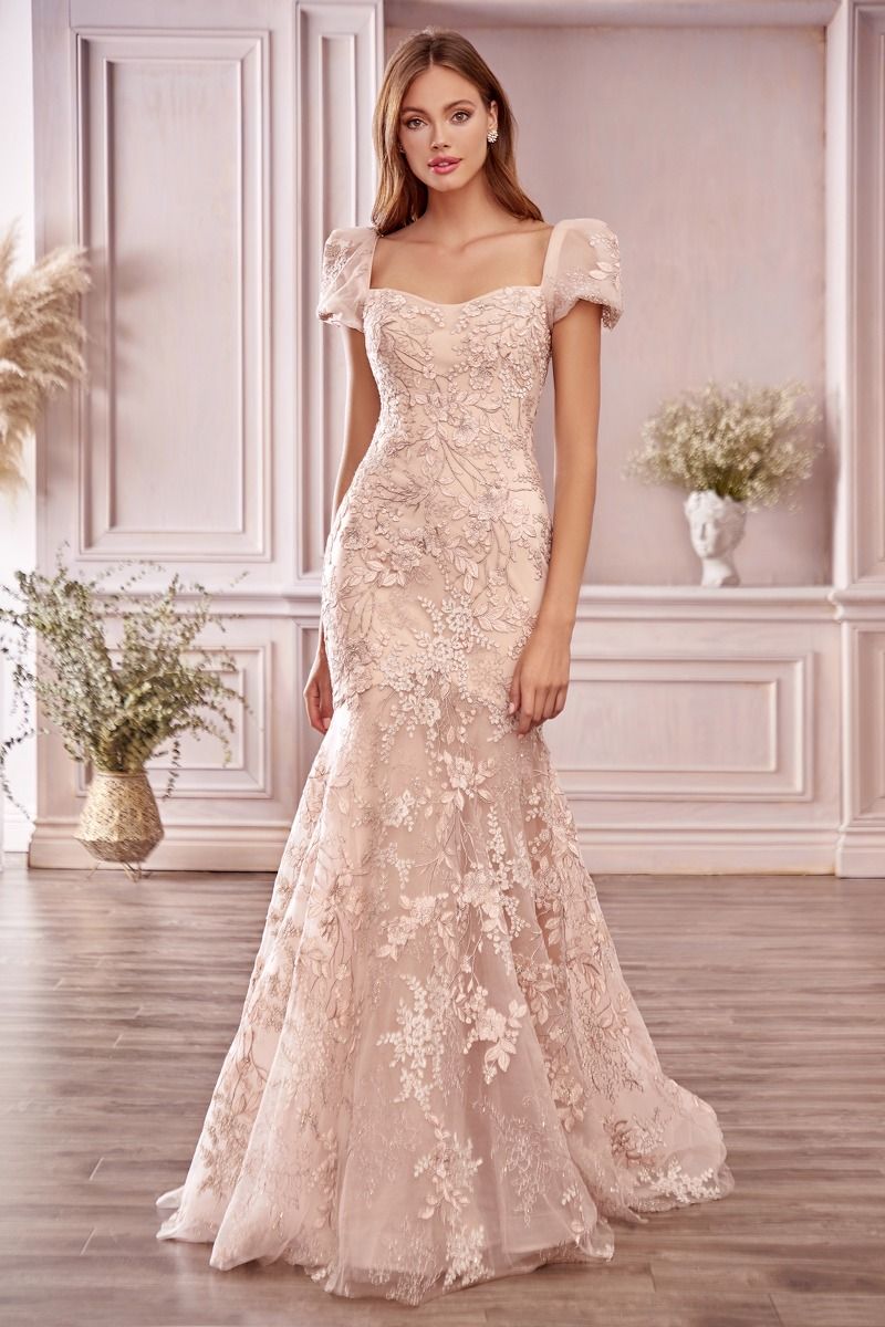 A woman stands indoors wearing the Long Pink Short-Sleeve Mermaid Prom Dress A1025, featuring floral lace detailing and puff sleeves for an elegant evening look.